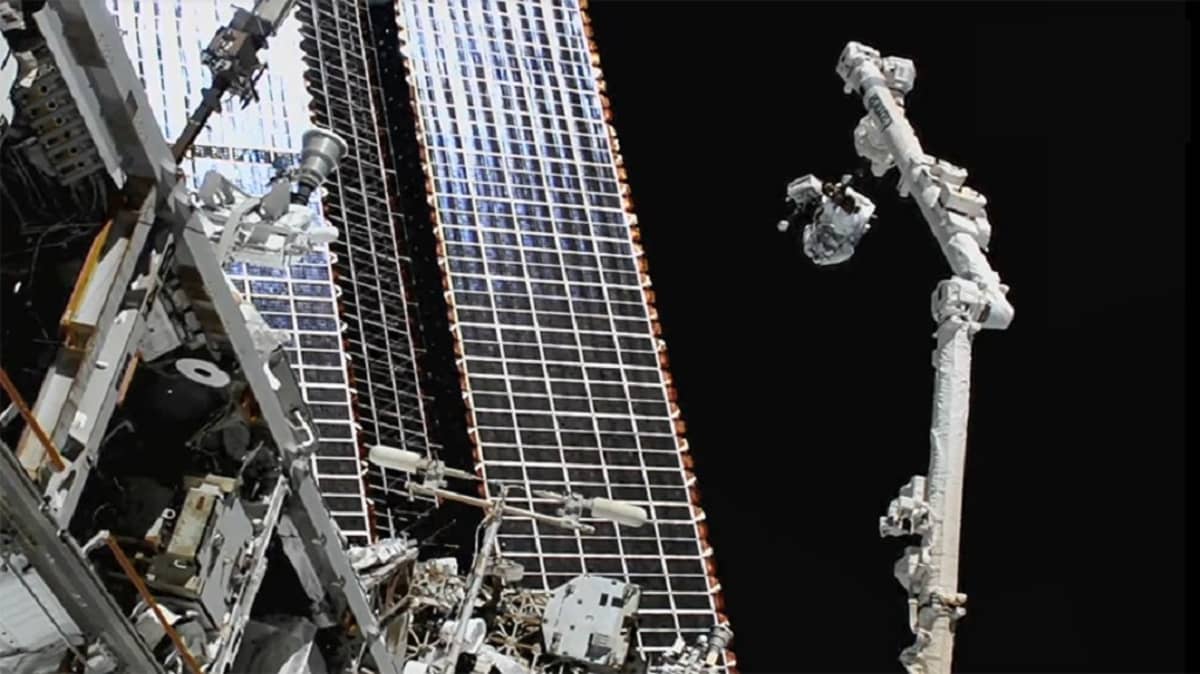 Osa ISS:ää ja siitä sojottava robottivarsi, johon on kiinnittynyt astronautti. 