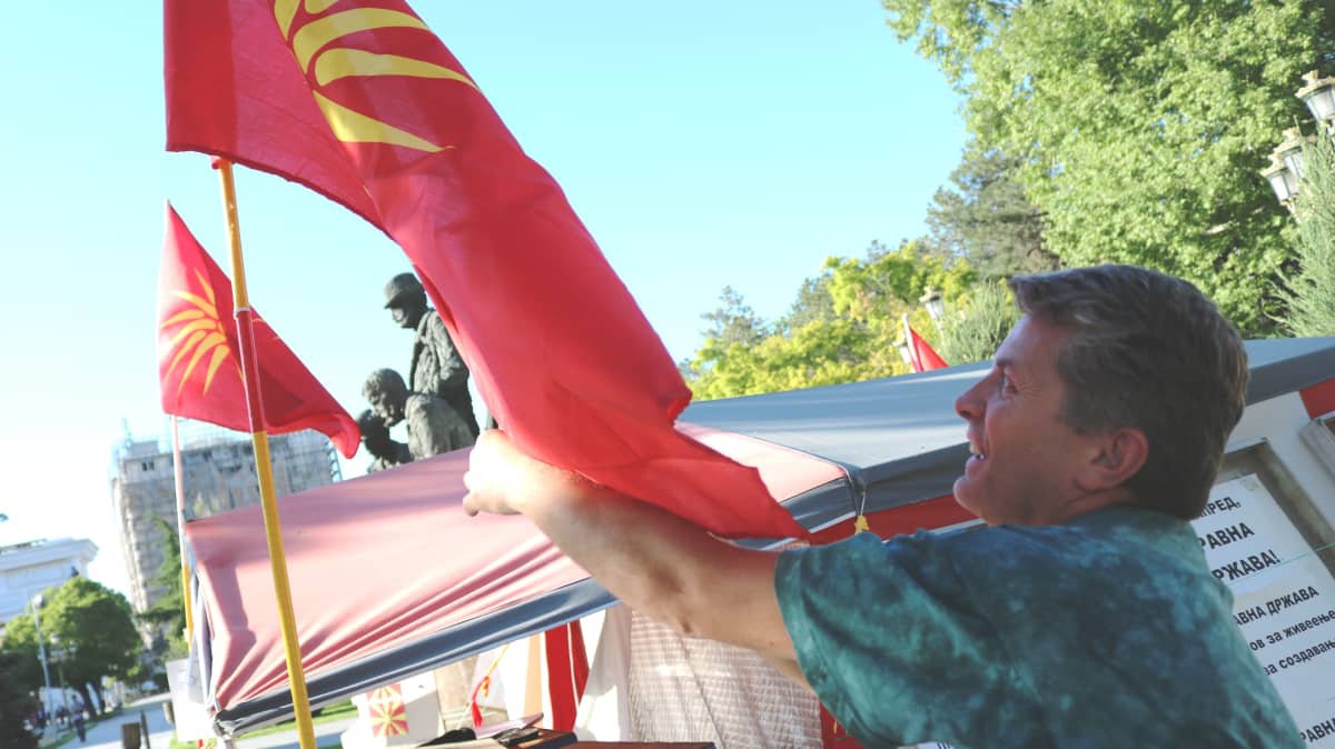 Goce Andjelkovski vastustaa Makedonian nimen muuttamista. Mielenosoitusleirissä liehuu Makedonian vanha lippu, jonka käytöstä luovuttiin 1990-luvulla koska se muistuttaa Kreikan puoleisen Makedonian maakunnan lippua.