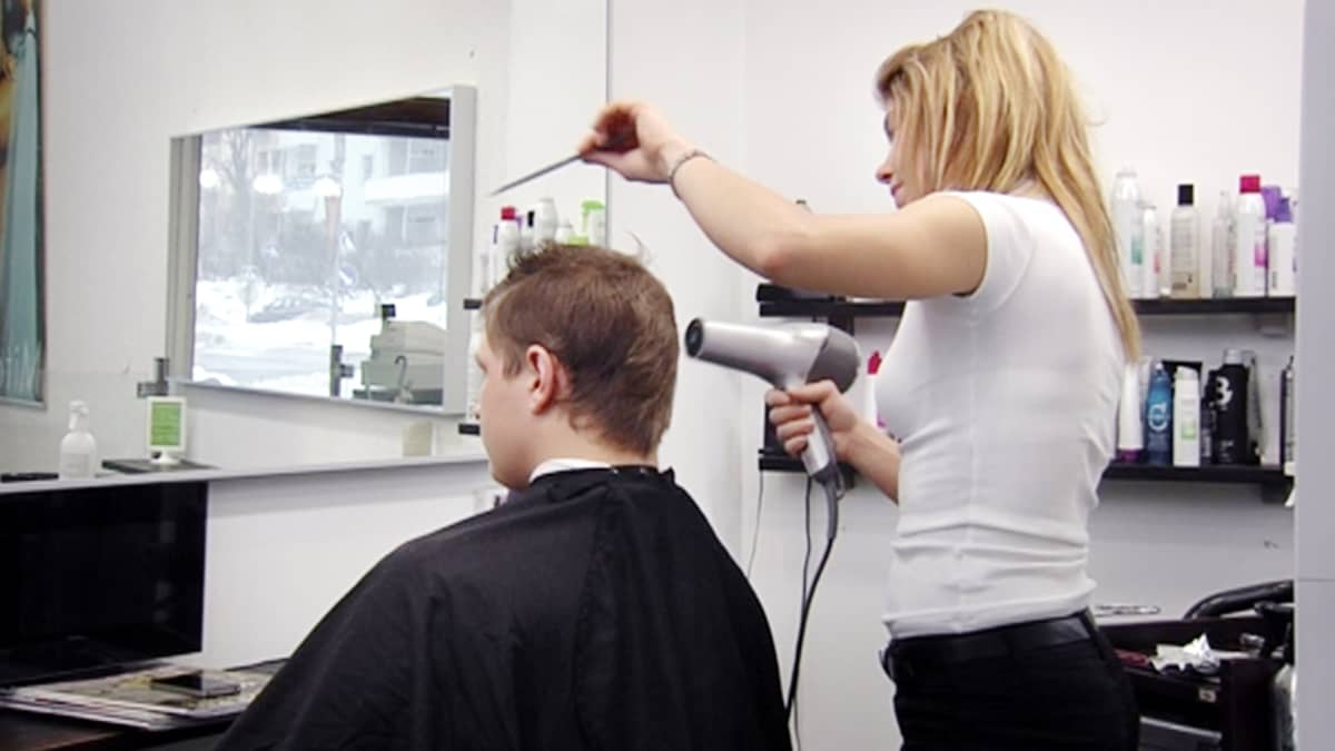 Parturi-kampaaja kuivaa asiakkaansa hiuksia.