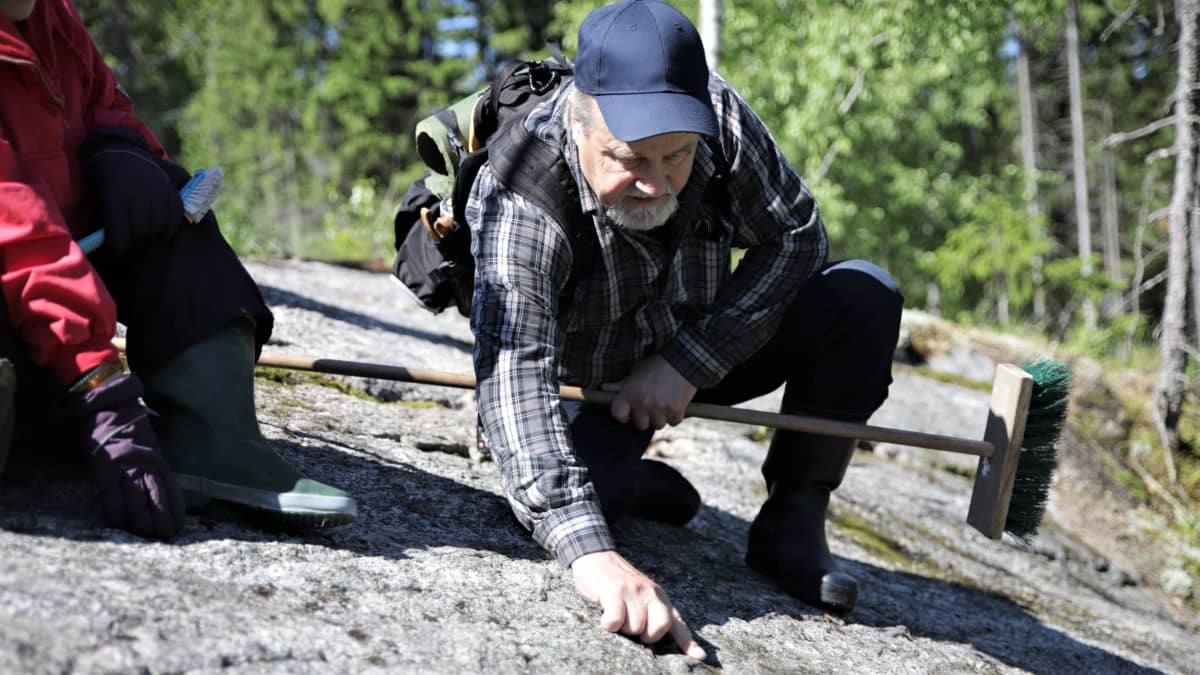 Arkeologian harrastaja Jukka Hietanen tutkii käärmekuviota kalliossa