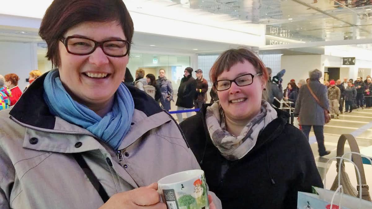 Tampere-talon aulassa kaksi hymyilevaa naista, joista toisella on uusi muumimuki kädessään