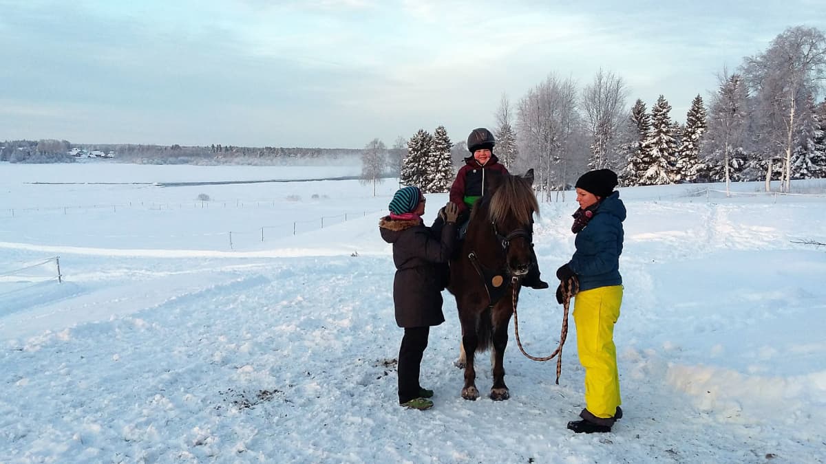 Einari Purra terapiahevosen selässä Torniojokivarressa. Apuna ratsastusterapeutti Lena Lassila, hevosesta huolehtii Jenni Ponkala.