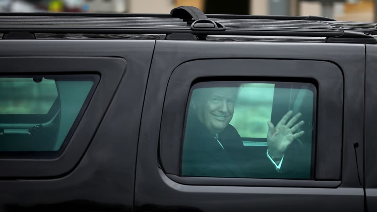 Trump vilkuttaa massiivisen mustan auton ikkunasta hymyillen leveästi.