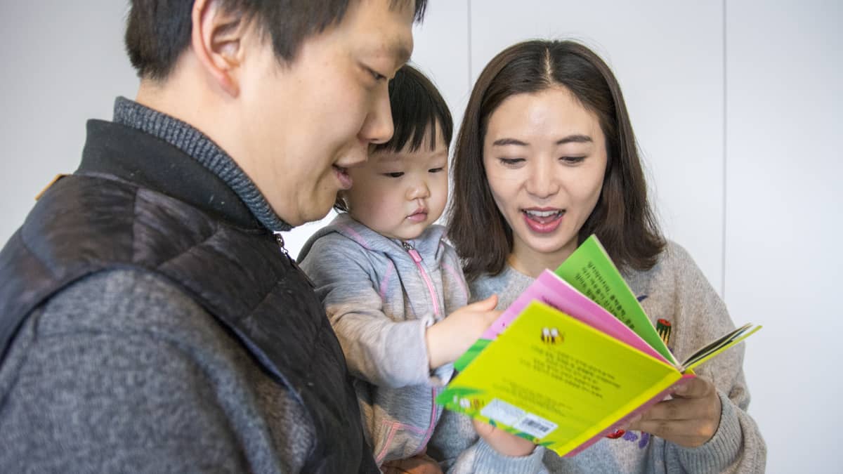Isä Hakhyun Kim, äiti Dami Park ja Seo Woo -vauva tutkivat lastenkirjaa.