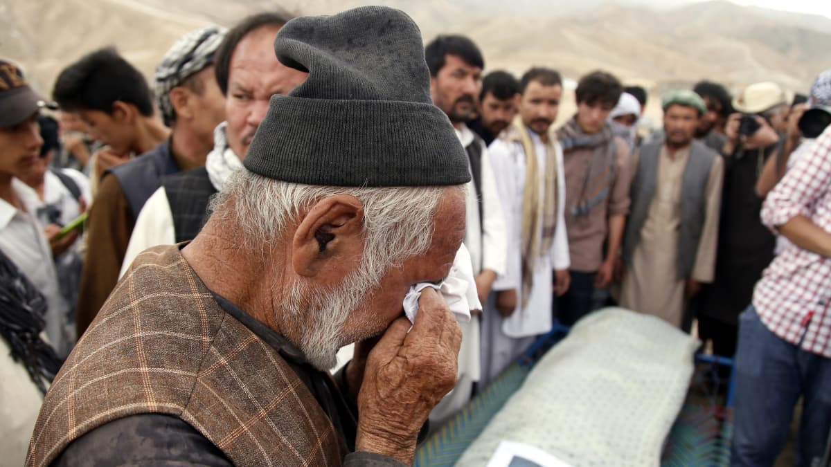 Kuvassa hazaramies itkee hautajaisissa. Taustalla muita miehiä.