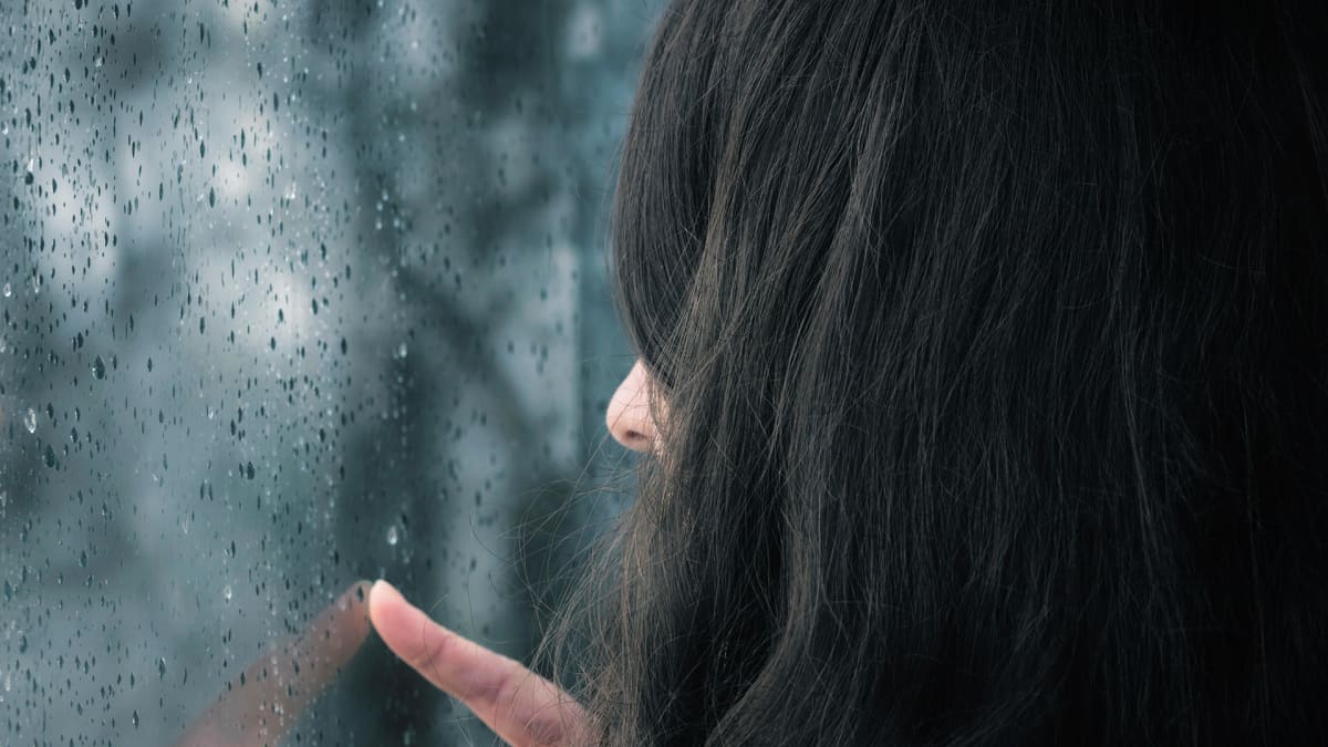 Naine katselee sateisen ikkunan läpi.