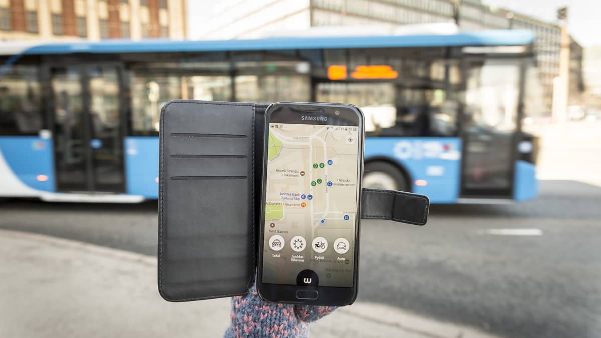 Whim-mobiilisovellus älypuhelimen näytöllä, taustalla linja-auto.