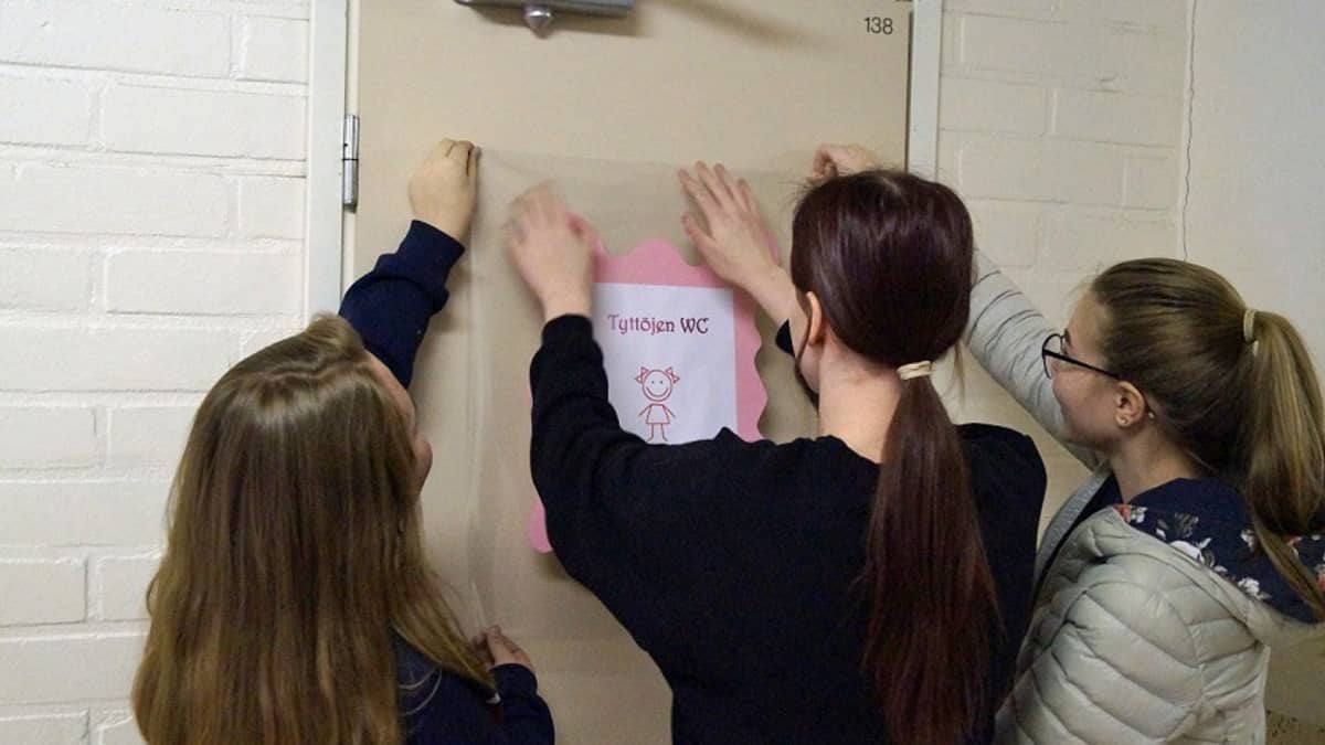Oppilaat kiinnittämässä merkkiä koulun vessan oveen.