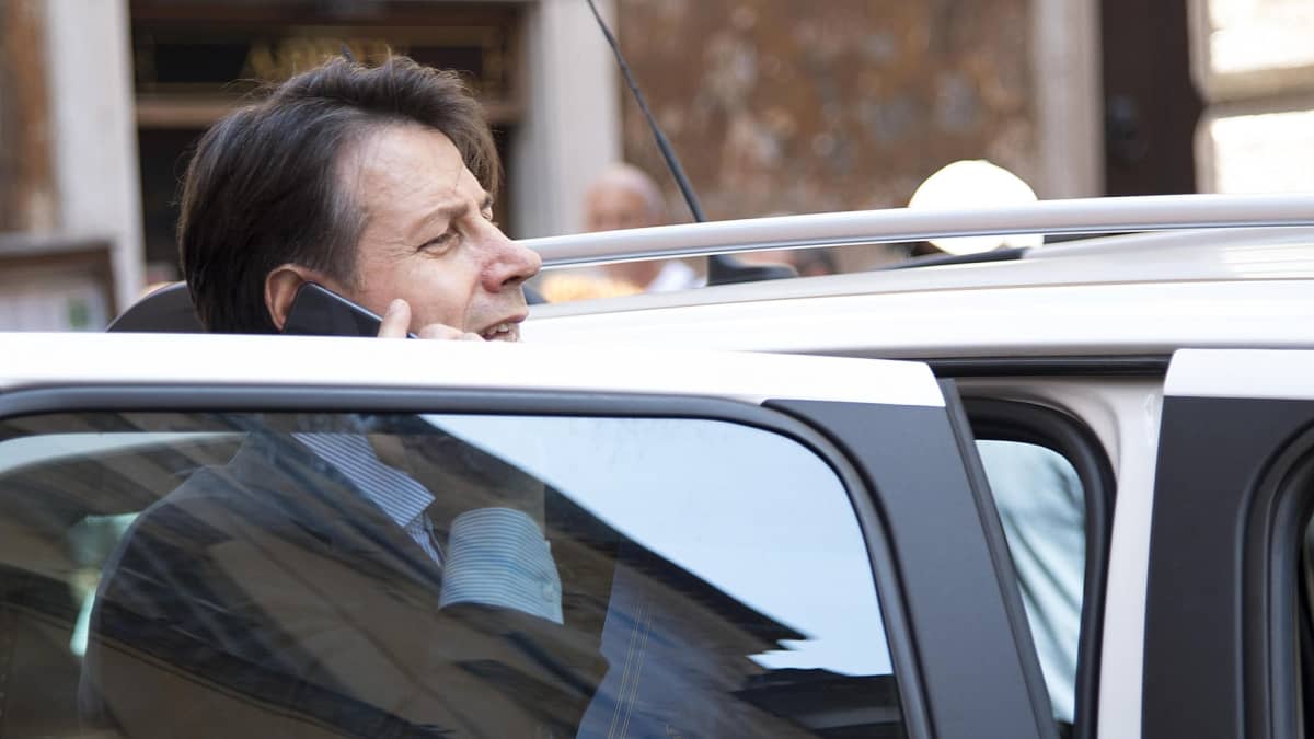 Kuvassa Giuseppe Conte on auton auki olevan oven takana puhumassa kännykkään.