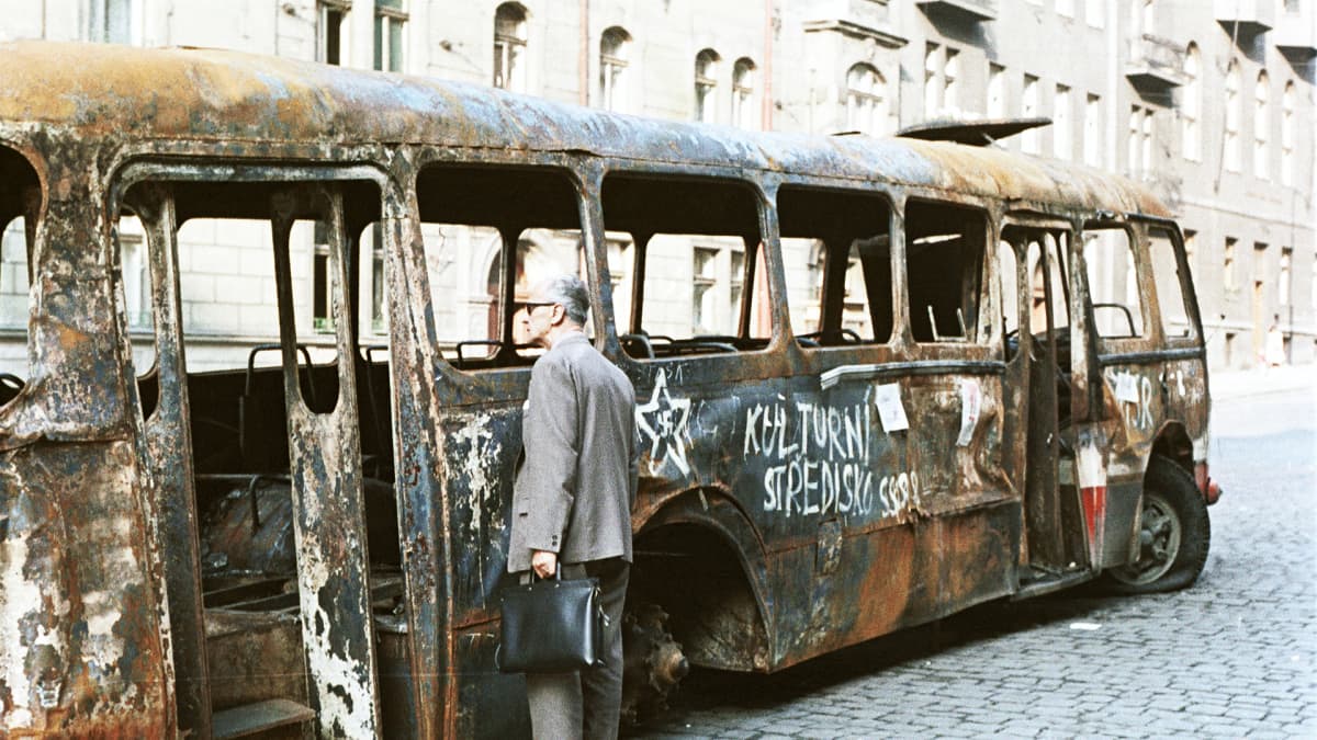 Prahalaismies tarkastelee neuvostovastaisilla iskulauseilla maalattua palaneen bussin hylkyä.