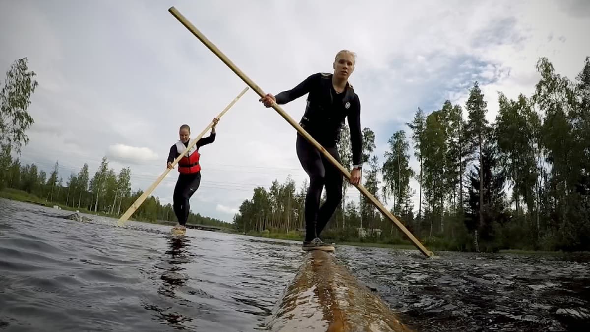 Iida Mäntylä ja Milla Sulkakoski tasapainoilevat tukkien päällä joessa.