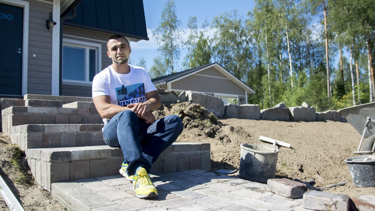 Nikoloz Dzutsovia istuu talon portailla. Taloon ollaan rakentamassa kivetys.