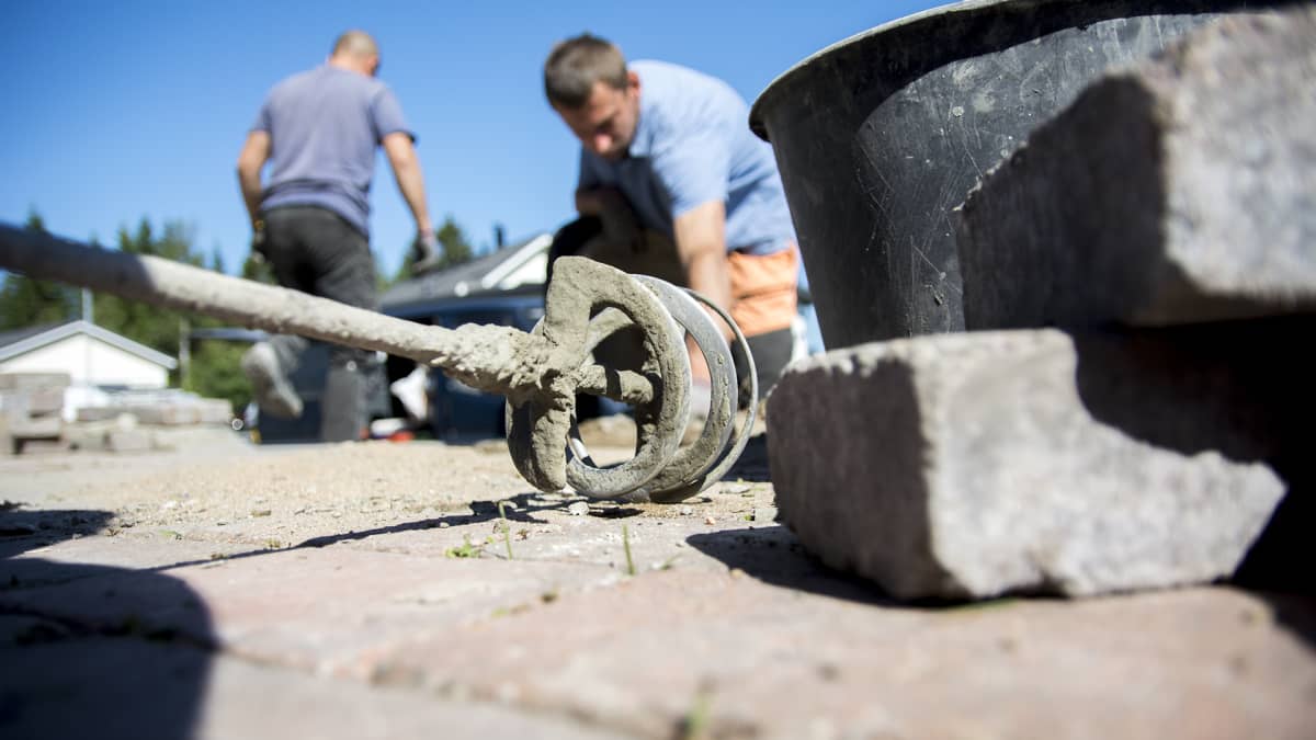 Etualalla työkaluja. Taustalla sumeana kaksi ukrainalaista työntekijää rakentamassa katukivetystä.