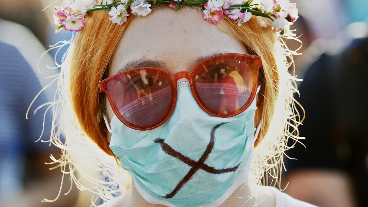 Mielenosoituksessa mukana oleva nainen on laittanut kukkaseppeleen päähän ja hengityssuojan suun eteen.
