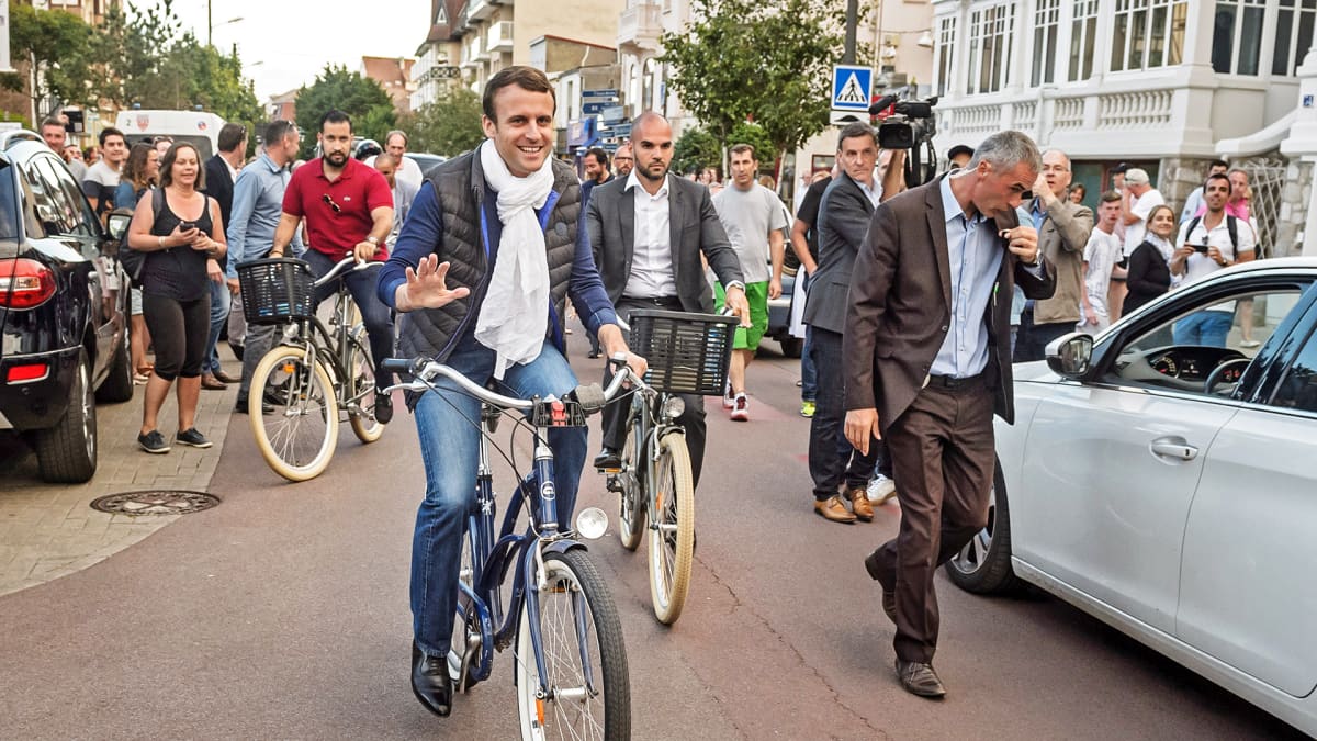 Emmanuel Macron pyöräilee kadulla.