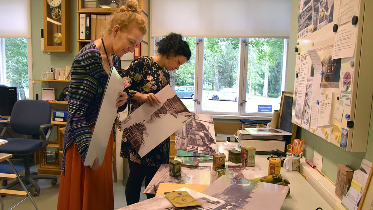 Kaksi naista tutkii valokuvatauluja museon toimistossa