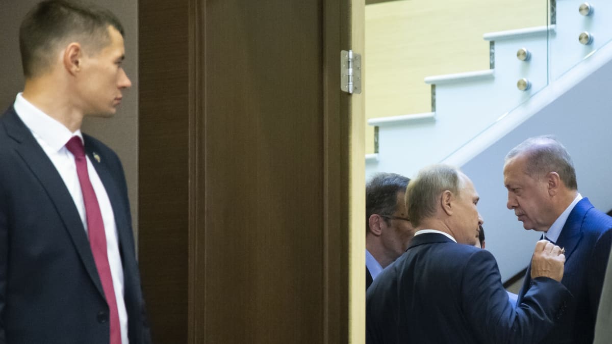 Venäjän presidentti Vladimir Putin ja Turkin presidentti Recep Tayyip Erdoğan keskustelevat kuvan oikeassa laidassa. Vasemmalla etualalla venäläinen henkivartija seisoo oven ulkopuolella.