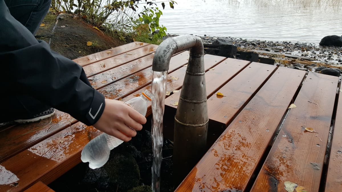 Henkilö ottaa vettä pulloon Lappeenrannan rantaraitin lähteeltä