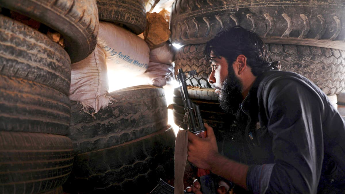 Syyrian kapinallistaistelija  tarkkailee etulinjaa autonrenkaista tehdystä suojasta.