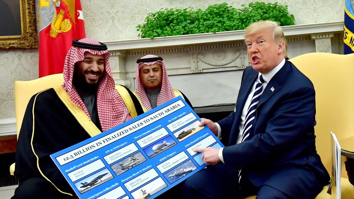 Mohammed bin Salman ja Trump istuvat tuoleilla. Trump osoittaa kädessään olevaa kuvaesitystä, jossa on kuvia muun muassa hävittäjistä ja sota-aluksista. Kruununprinssi nauraa.