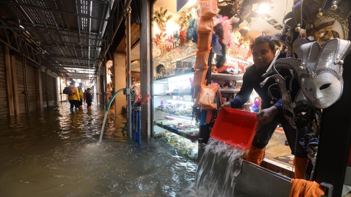 Mies tyhjentää tulvavesien valtaamaa liiketilaansa Venetsiassa 29. lokakuuta 2018.