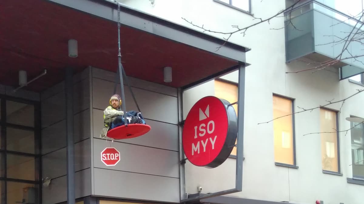 Mielenosoittaja roikkuu kauppakeskuksen sisäänkäynnin yläpuolella Joensuussa.