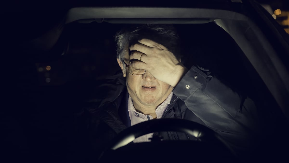 Juha Rehula istuu autossa pimeyden keskellä käsi otsalla.