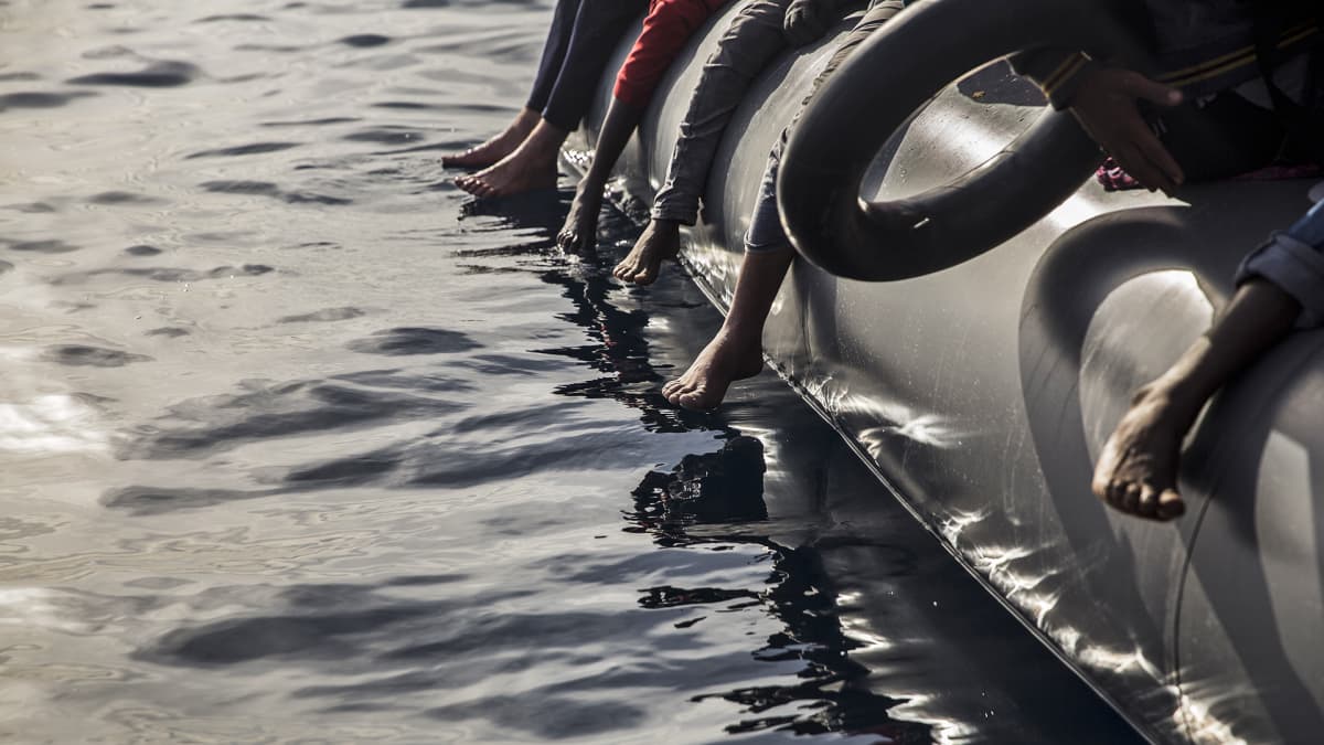 Pakolaisten jalkoja pelastusveneen reunalla.
