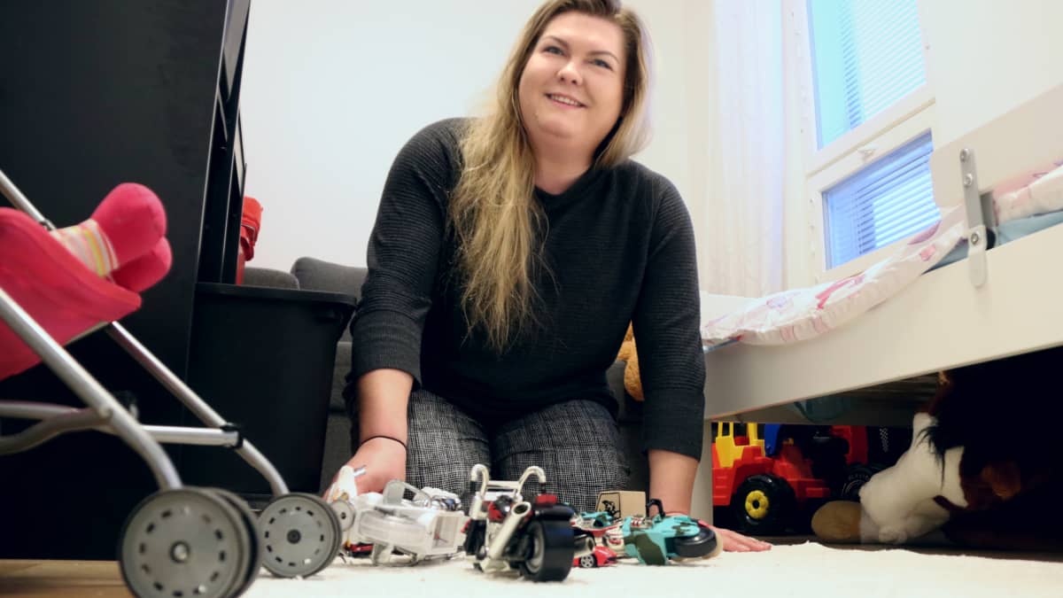 Krista Krubally istuu lasteenhuoneen lattialla ja kerää leluja.
