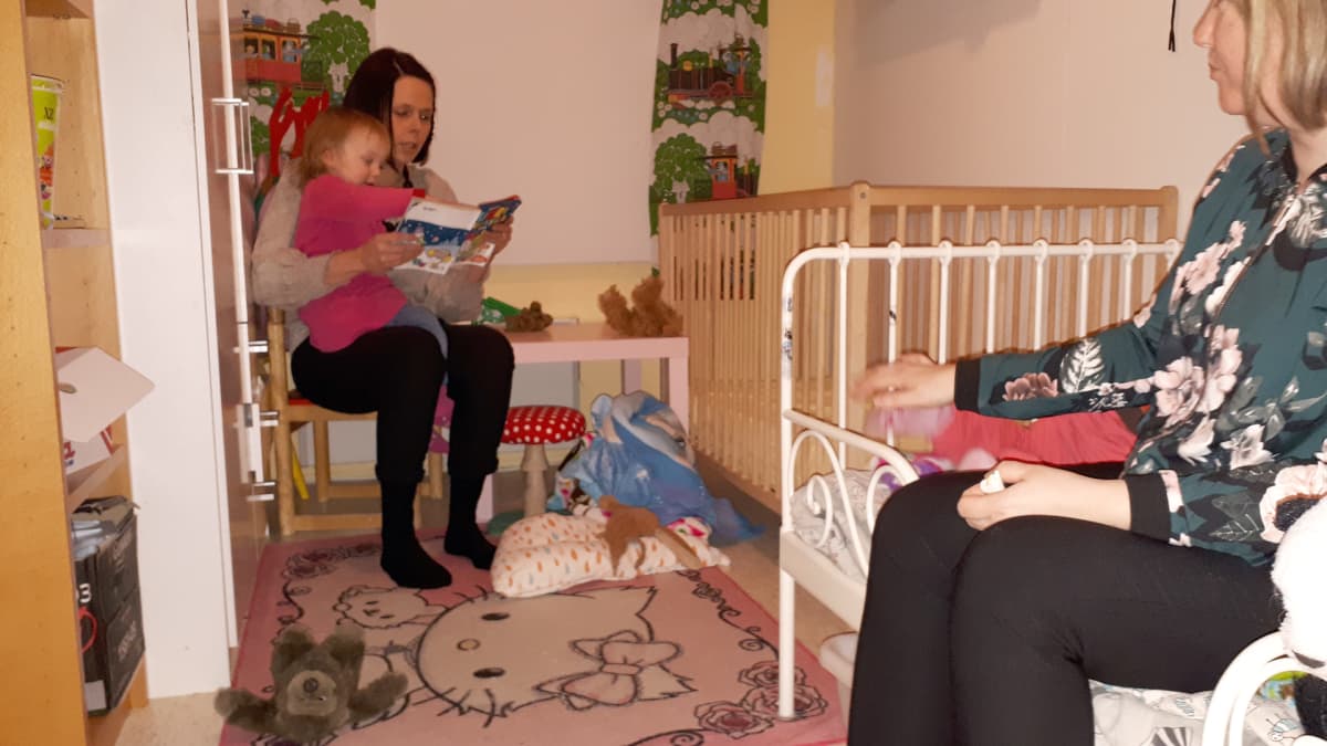 Lapsi ja nainen lukevat kirjaaa lastenhuoneessa, nainen seuraa sivummalla.