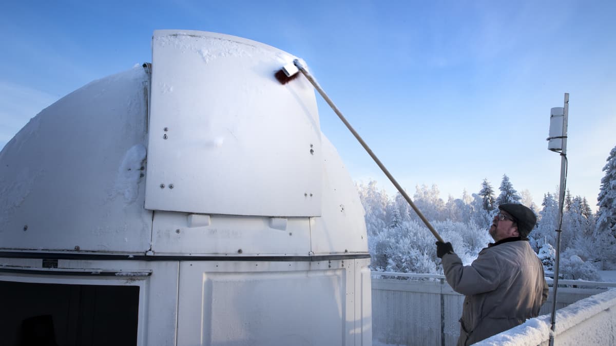 Mies harjaa observatorion luukusta lunta.