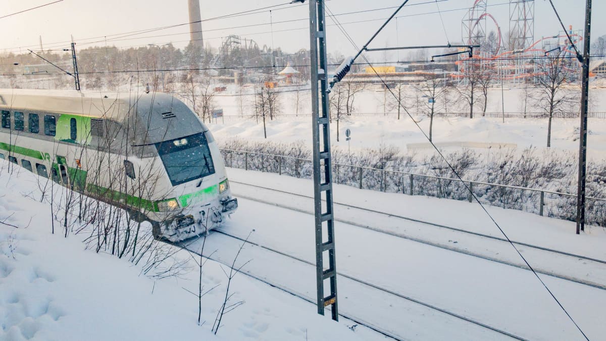 Juna ajaa lumisella radalla Tampereen Näsinkallion kupeessa