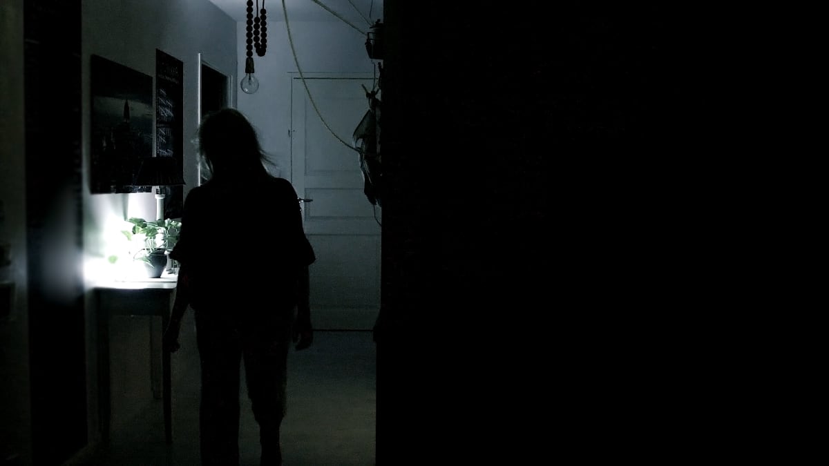 Nainen kävelee pimeässä asunnossa yöllä.