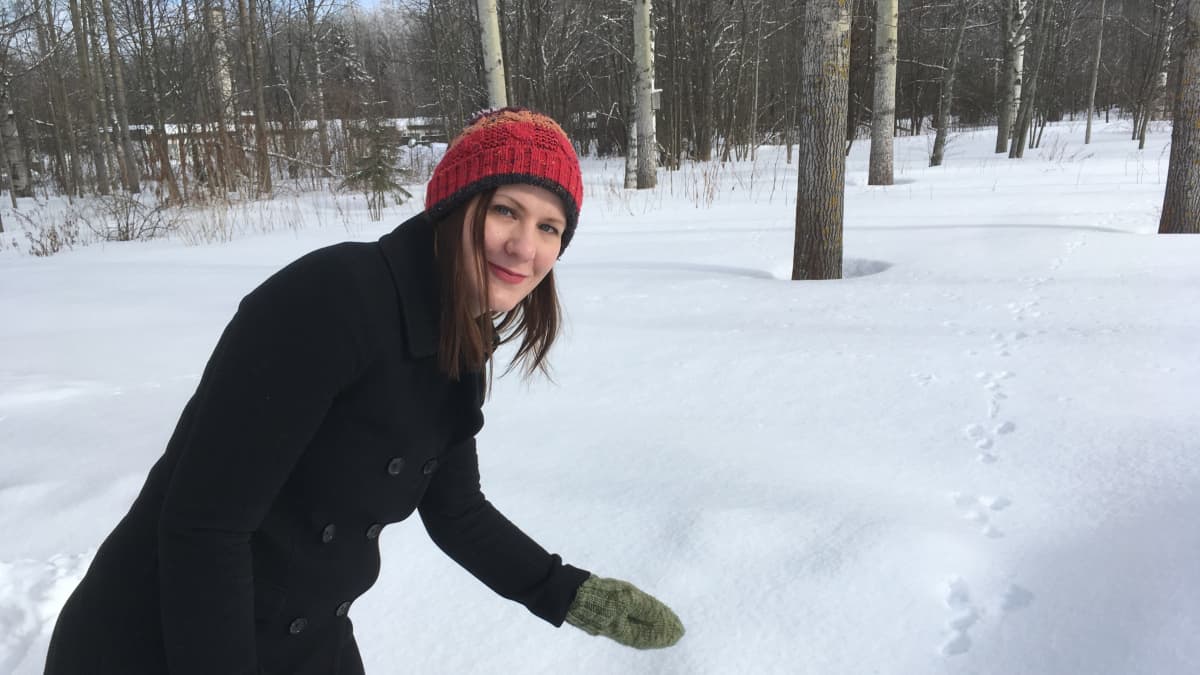 Väitökirjatutkija Riikka Levänen lumisessa metsässä rusakon jälkien ääressä.