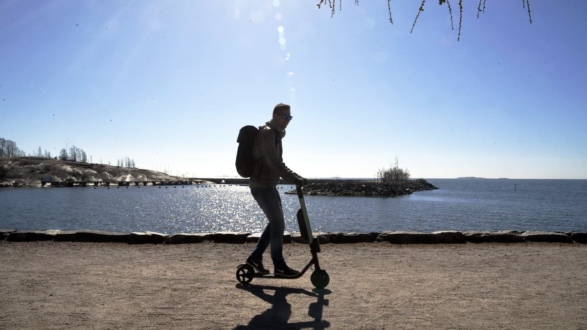  Mies vauhdissa sähköpotkulaudalla lämmittävässä kevätauringossa Helsingin Merisatamassa