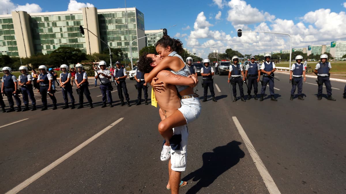 Nais- ja miesprotestoija suutelevat kiihkeästi poliisien edessä vastustaen Brasilian presidentti Jair Bolsonaron koulutusleikkauksia.