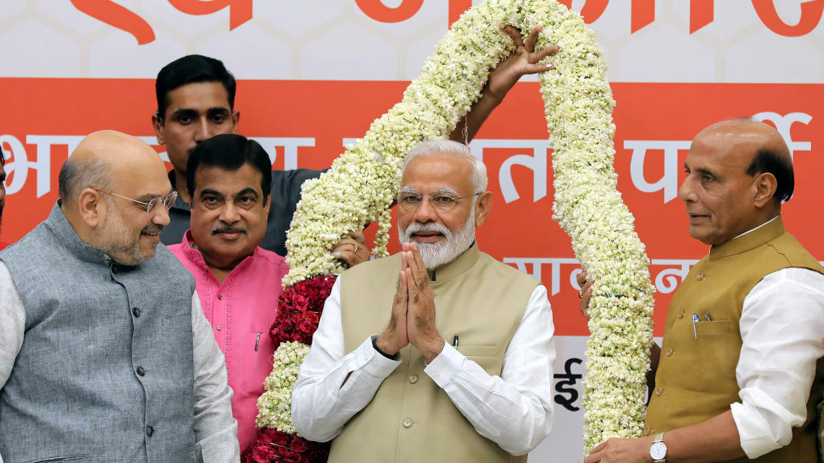 Pääministeri Narendra Modi seisoo puoluetovereidensa ympäröimänä. Taustalla suuri kukkaköynnös.