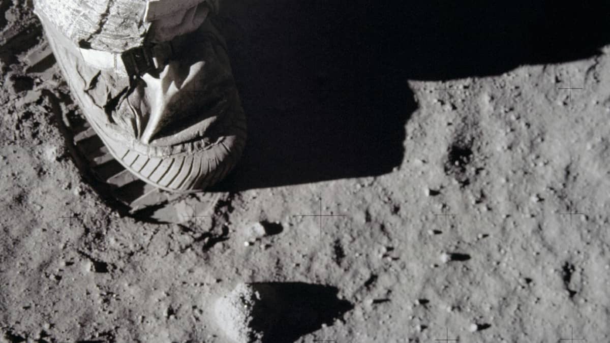 Astronautin jalka painamassa jälkeä Kuun pölyiseen pintaan. 