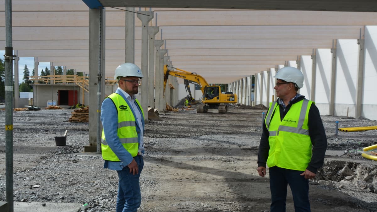 Kaksi miestä seisoo liivit päällä rakennustyömaalla