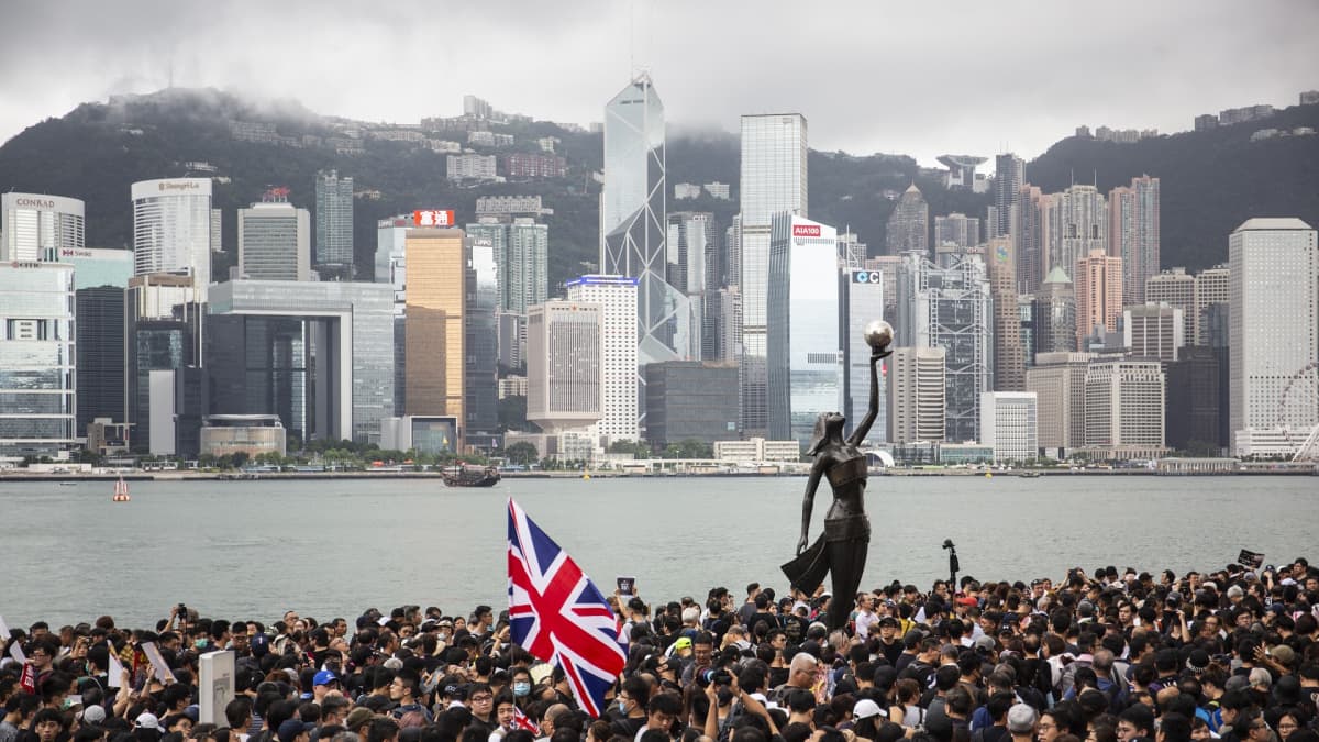 Valtava ihmisjoukko. Keskellä patsas. Taustalla Hongkongin pilvenpiirtäjiä.