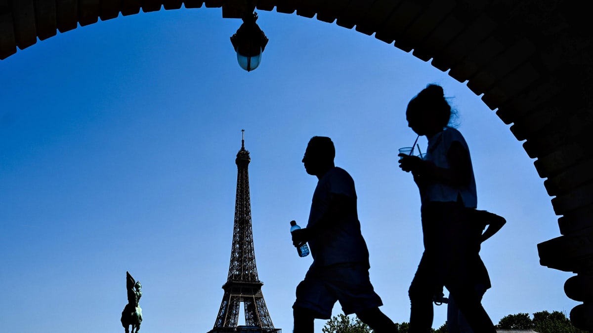 Siluettikuvassa mies pitää vesipulloa ja nainen juo pillillä muovilasista Eiffel-tornin lähistöllä Pariisissa.