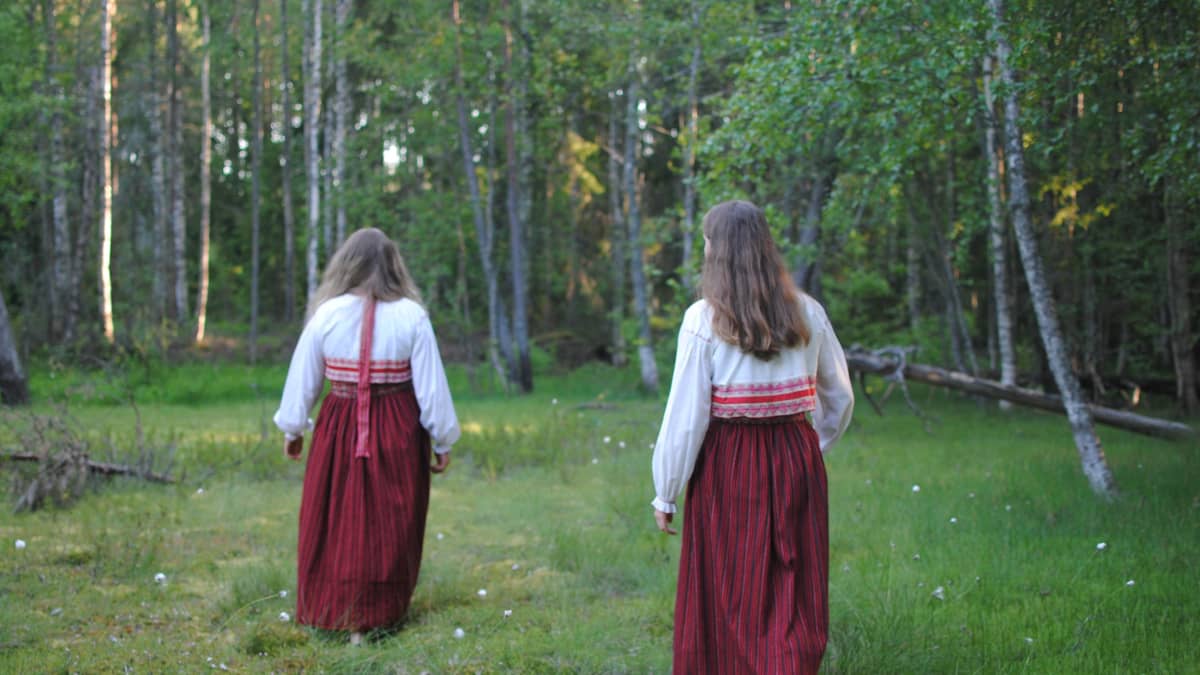 Lumi Rinne ja Säde Rinne kävelevät poispäin kamerasta Lavansaaren kansallispuvut yllään. 