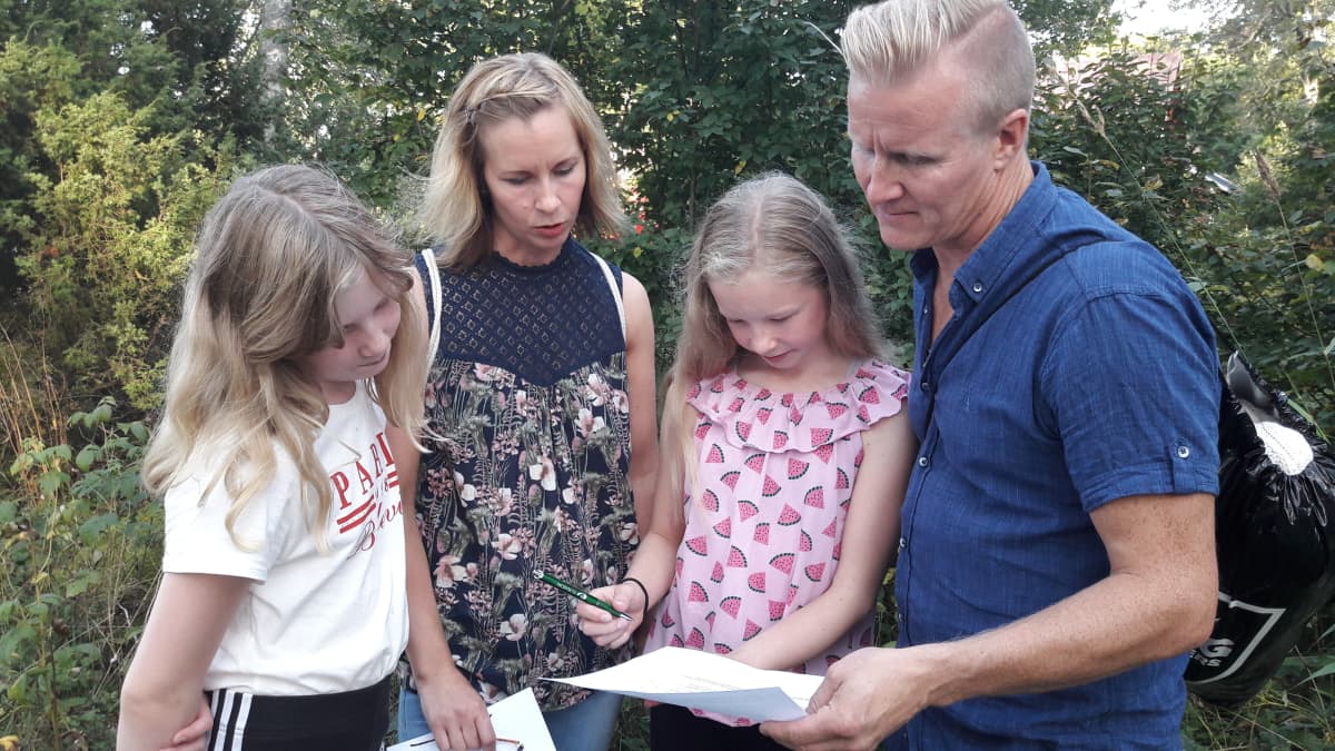 Isä, äiti ja kaksi tytärtä lukevat paperia