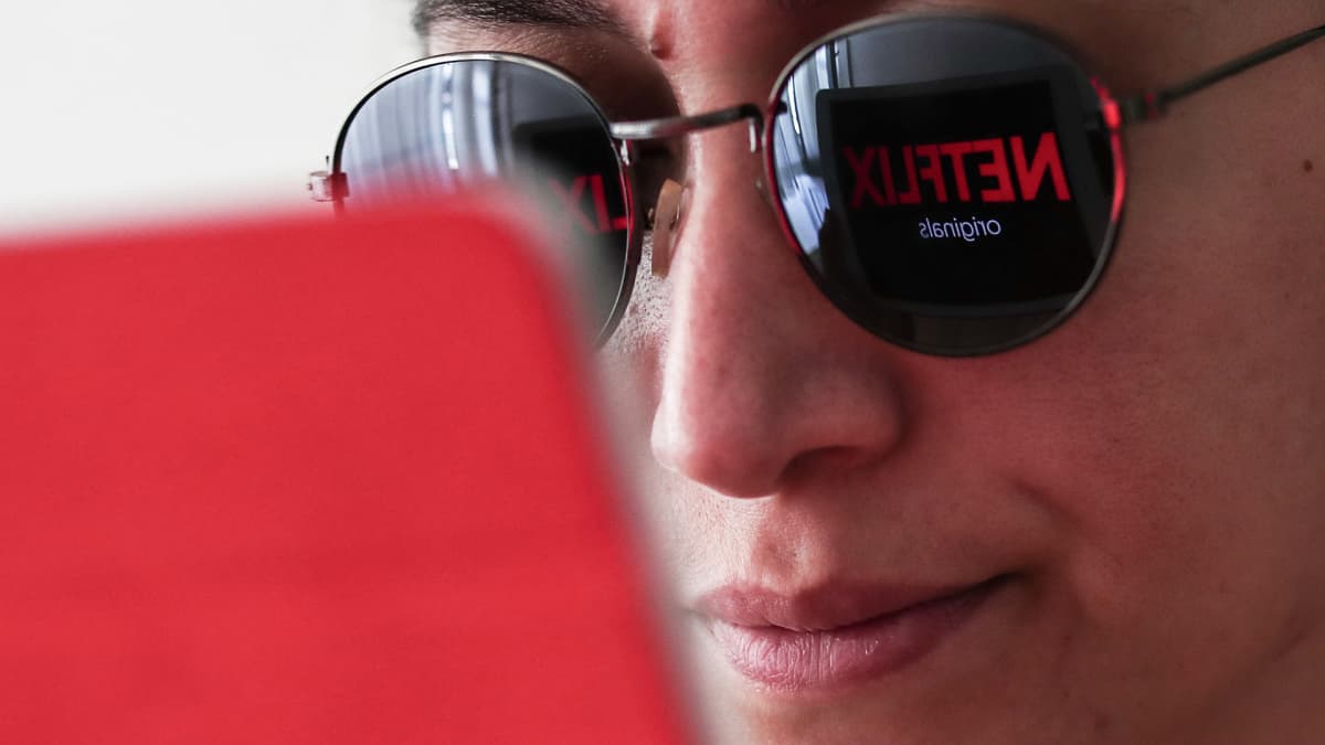 Netflix-logo heijastuu läppärin näytöltä naisen aurinkolaseihin.