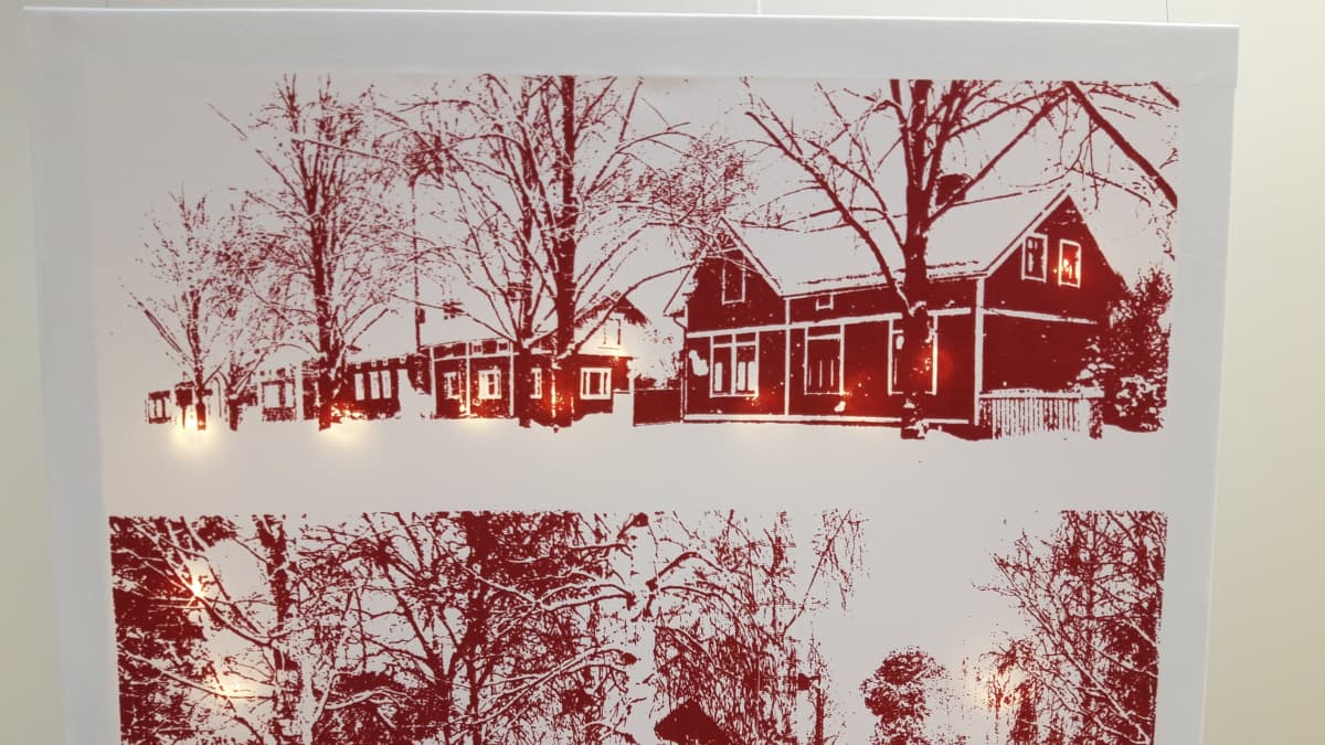 Valotaulu, missä punavalkoinen talomaisema, ja ledvalot loistavat kankaan takaa talojen ikkunoista.
