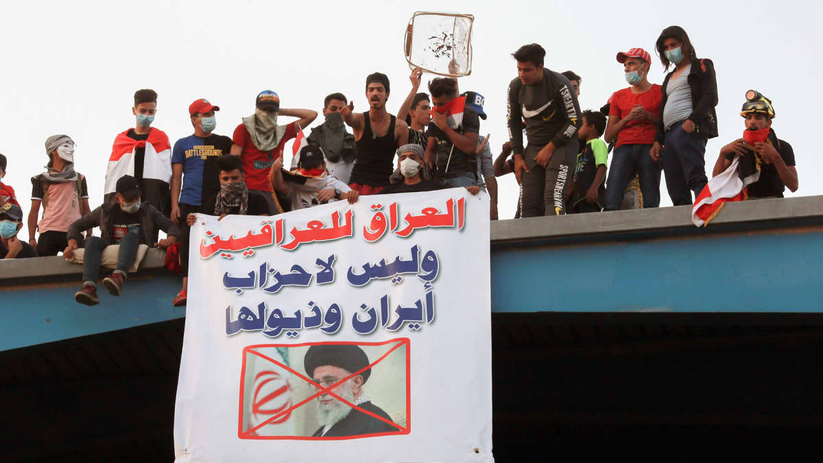 Irakilaisia mielenosoittajia roikottavat banneria sillalta jossa on Iranin Khamenein kuva. 