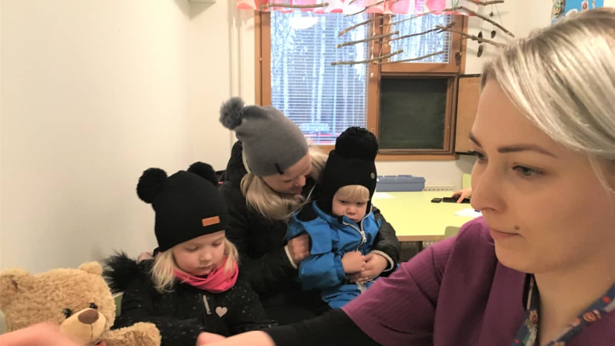 Terveydenhoitaja Siiri Vuorinen valmistelee influenssarokotteita päiväkodissa. Pinja, Emmi ja Perttu Hirvonen odottavat vuoroaan.