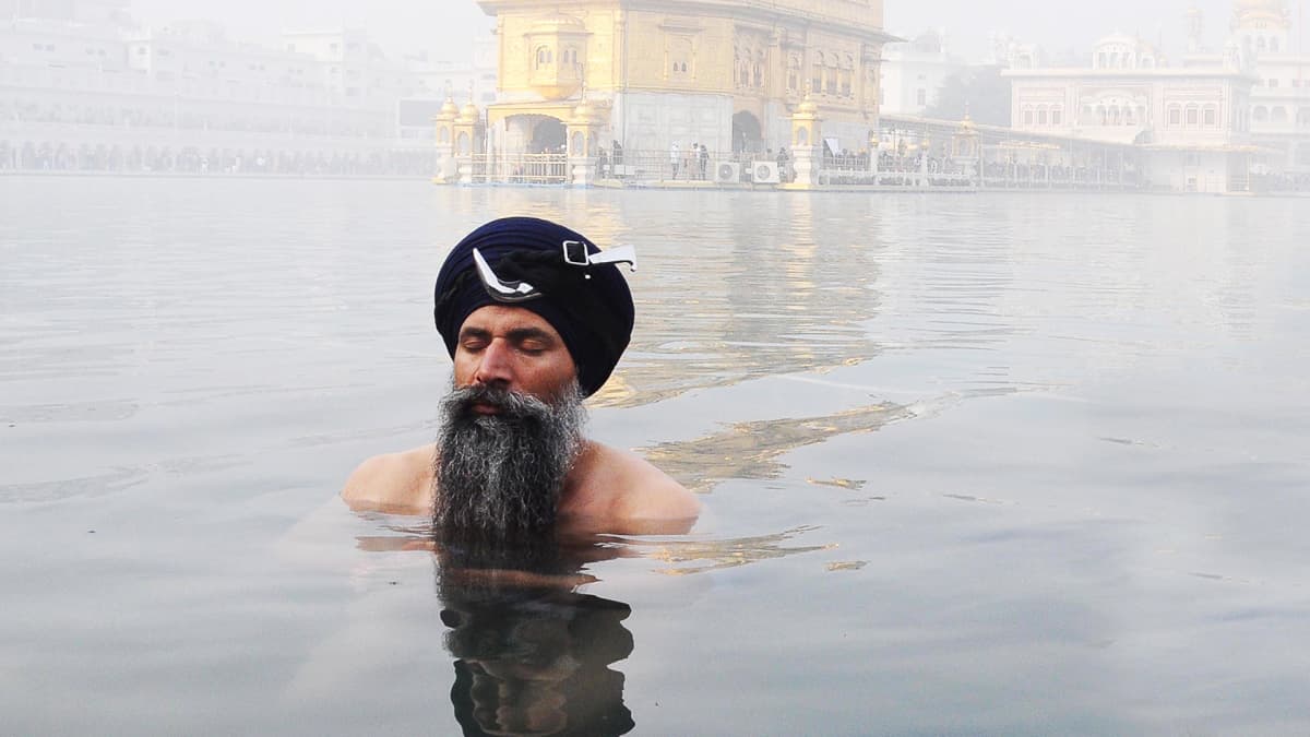Mies kylpee Kultaisen temppelin pyhässä vedessä Amritsarissa, Intiassa.