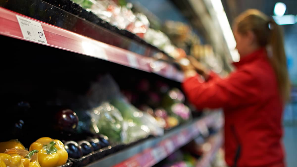 Työntekijä täyttää vihanneshyllyä supermarketissa.