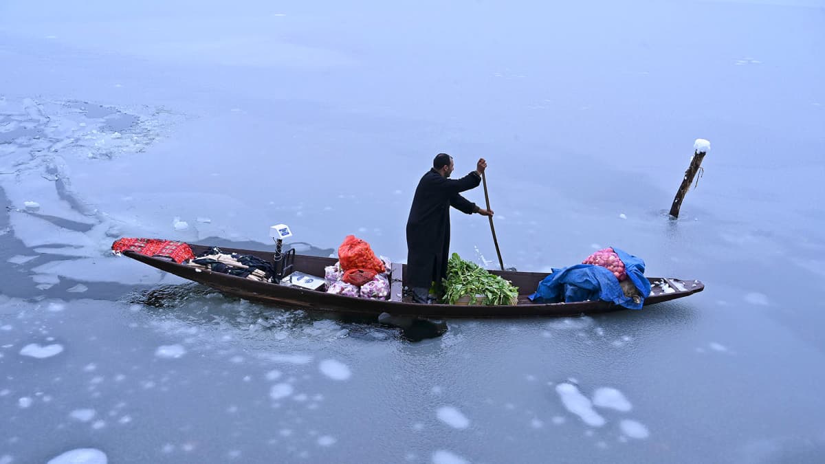 Mies kuljettaa veneellä vihanneksia jäätyneessä Dal-järvessä.